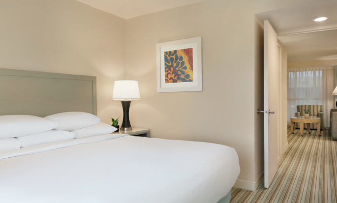 Dormitorio privado bien iluminado en la suite con cómoda cama King y vista al área del lounge.